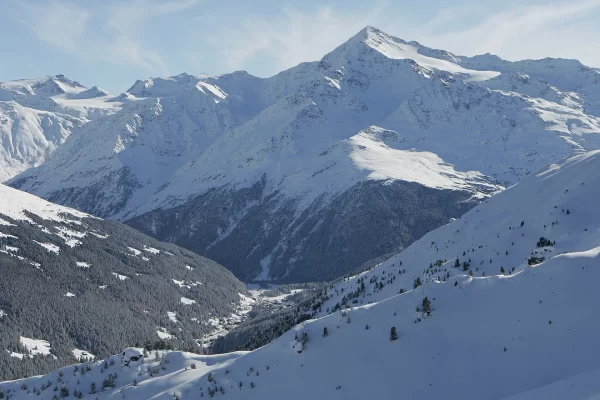 Panorama montano innevato con cielo azzurro e valli coperte di neve.